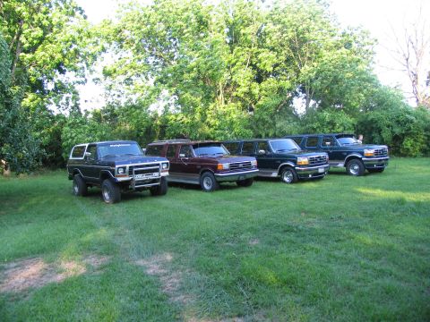 1995 Ford C-350 (Centurion Conversions) - A lineup of four SUVs, including a dark blue and white Bronco, a maroon extended SUV, and two dark green extended SUVs.