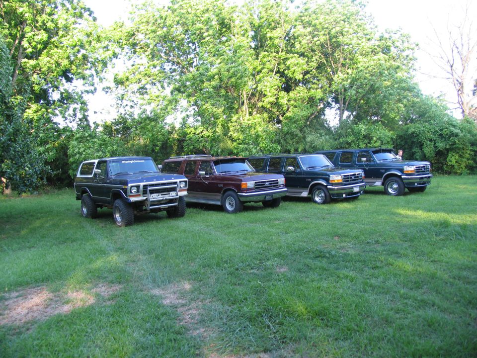 Four SUVs parked in a row, three are dark green and one is maroon. The front SUV has a white top