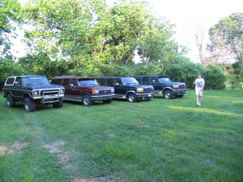 1995 Ford C-350 (Centurion Conversions) - A lineup of four Ford SUVs, possibly Broncos and Centurions, parked on a lawn with trees in the background.