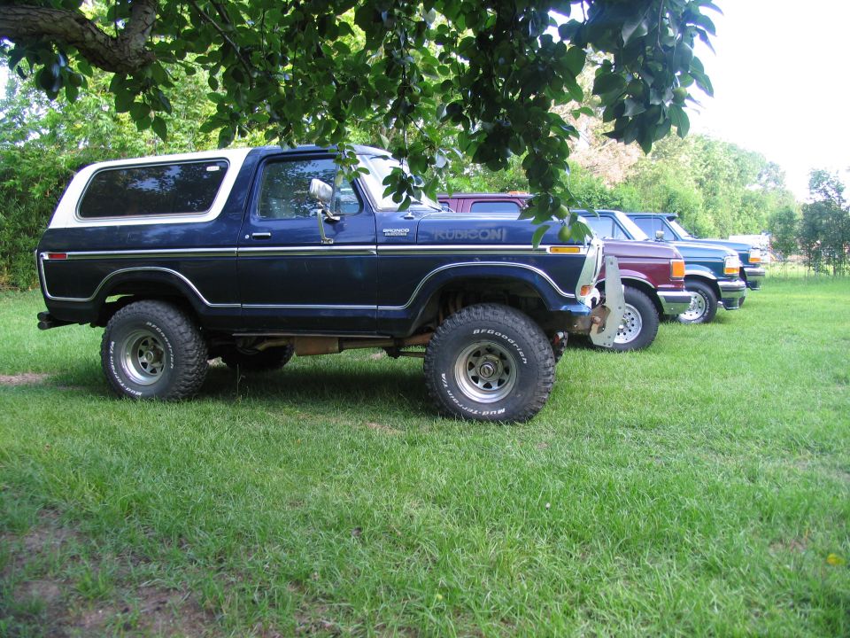 Dark blue Ford Bronco with white top, parked in grass next to other trucks. "REDCON" text visible on side