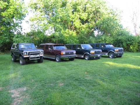 1995 Ford C-350 (Centurion Conversions) - A line of four SUVs are parked on a grassy lawn with trees in the background.