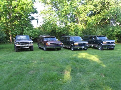 1995 Ford C-350 (Centurion Conversions) - Several Ford SUVs are parked on a grassy lawn with trees in the background.