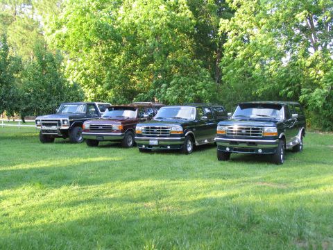 1995 Ford C-350 (Centurion Conversions) - Four SUVs, likely from the early to mid-1990s, are parked in a line on a grassy area with trees behind them.