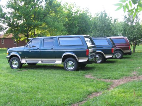 1995 Ford C-350 (Centurion Conversions) - Three extended Ford Bronco SUVs are lined up on a grassy lawn with trees in the background.