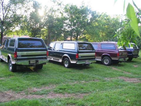 1995 Ford C-350 (Centurion Conversions) - Multiple Ford Bronco Centurion Conversions SUVs are parked in a grassy area with trees in the background.