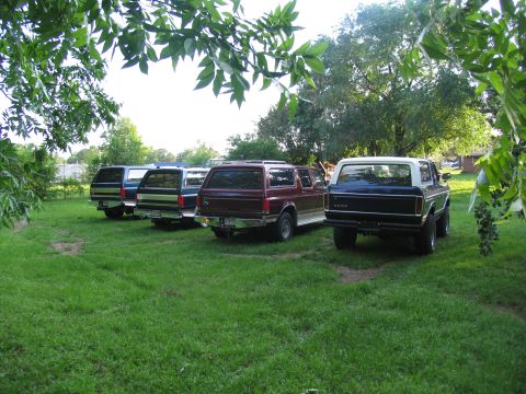 1995 Ford C-350 (Centurion Conversions) - Several Ford Broncos and extended Broncos are parked on a lawn under trees.