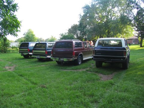 1995 Ford C-350 (Centurion Conversions) - Multiple SUVs are parked in a grassy area, with trees and a house in the background.