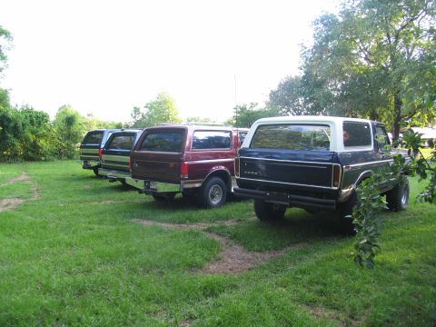 1995 Ford C-350 (Centurion Conversions) - Four Ford Broncos are lined up in a grassy yard, showing their rear ends.