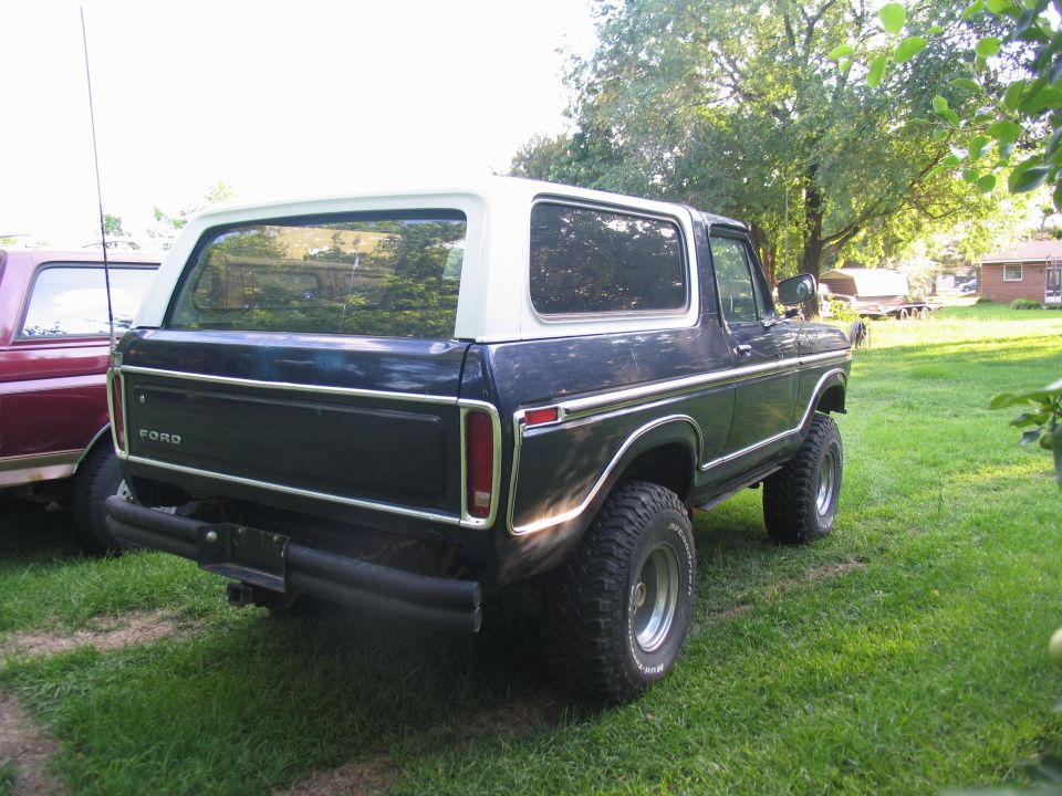 Dark blue Ford Bronco with white top, parked on grass next to a red vehicle