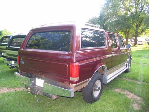 1995 Ford C-350 (Centurion Conversions) - A maroon Ford Bronco conversion is parked in a grassy area next to another vehicle.