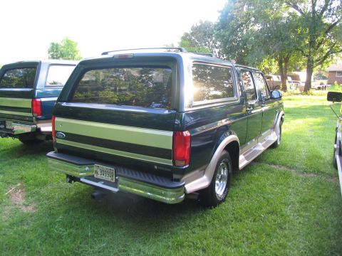 1995 Ford C-350 (Centurion Conversions) - Rear view of a dark green Ford Bronco with tan trim, parked on grass next to another similar vehicle.