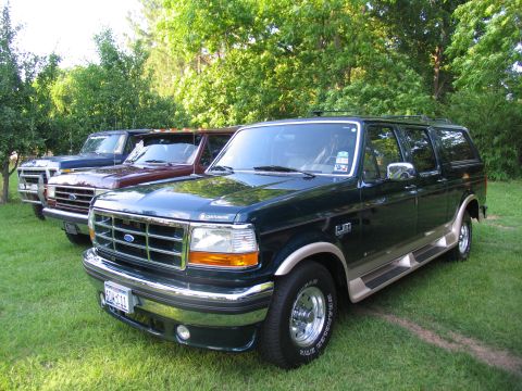 1995 Ford C-350 (Centurion Conversions) - Three SUVs are parked in a grassy area with trees in the background. The front vehicle is a dark green Ford Bronco.