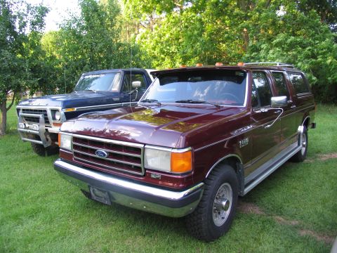 1995 Ford C-350 (Centurion Conversions) - A maroon Ford F-Series truck is parked on a grassy lawn next to a blue Ford F-Series truck.