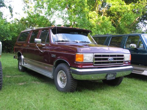 1995 Ford C-350 (Centurion Conversions) - A maroon Ford Bronco SUV is parked on a grassy lawn with trees in the background.