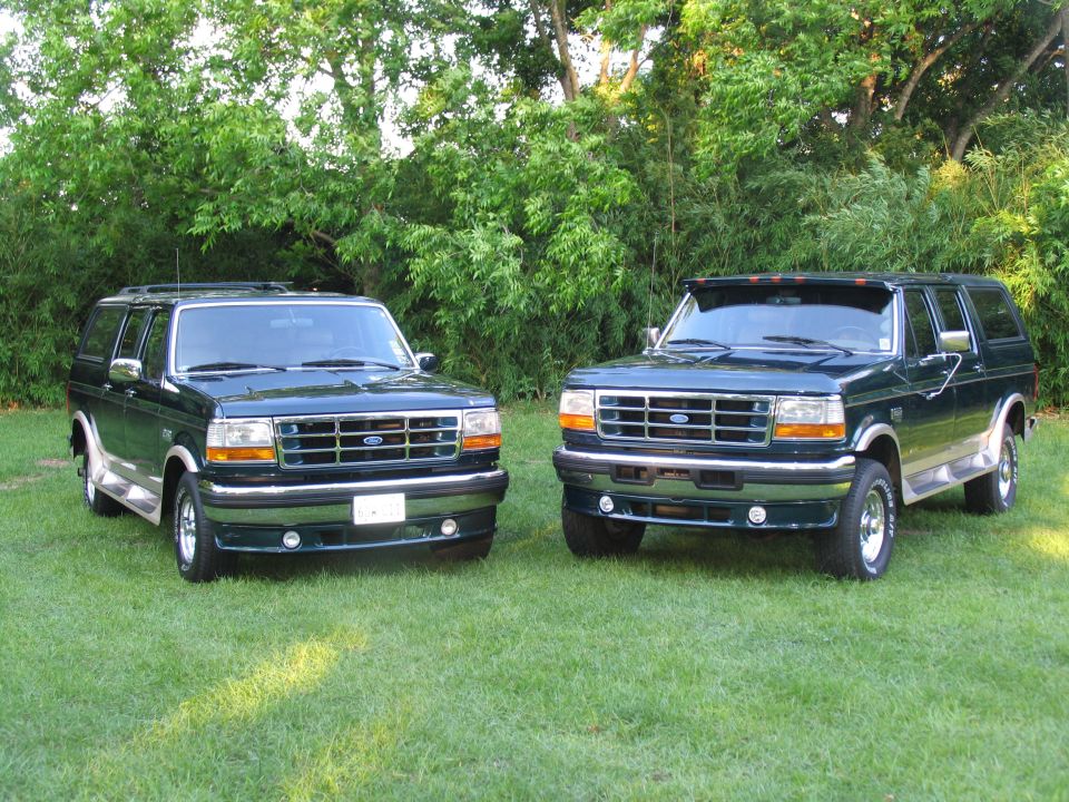 Two dark green Ford Bronco/F-Series SUV conversions parked on grass, front 3/4 view