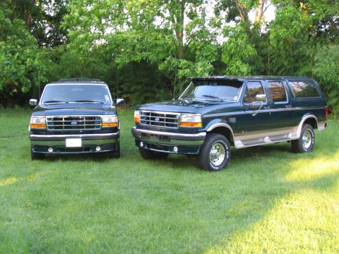 1995 Ford C-350 (Centurion Conversions) - Two dark green Ford SUVs with tan lower body trim are parked on a grassy lawn with trees in the background.