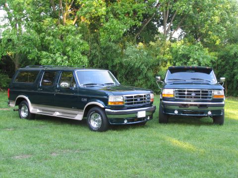 1995 Ford C-350 (Centurion Conversions) - Two dark green Ford SUVs, one a Centurion Conversion, parked on a grassy lawn with trees behind them.
