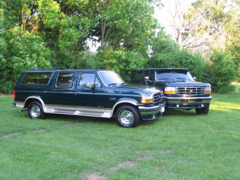1995 Ford C-350 (Centurion Conversions) - Two dark green Ford SUV conversions with tan lower trim are parked on a grassy lawn with trees in the background.