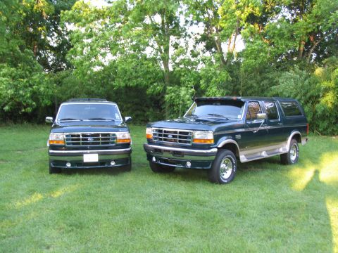 1995 Ford C-350 (Centurion Conversions) - Two dark green Ford SUVs are parked on a grassy lawn with trees in the background.