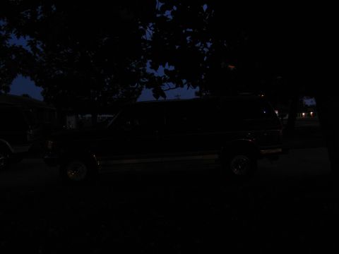 1995 Ford C-350 (Centurion Conversions) - A dark-colored SUV is parked outdoors at dusk, with trees partially obscuring the view.