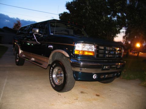 1995 Ford C-350 (Centurion Conversions) - A dark green Ford Bronco is parked on a concrete driveway with trees in the background.