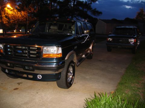 1995 Ford C-350 (Centurion Conversions) - Two SUVs are parked in a driveway at twilight, with a street light illuminating trees in the background.