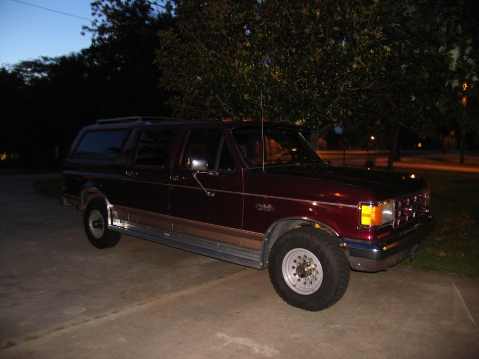 Maroon Ford conversion SUV with tan cladding parked on driveway at dusk, 3/4 front view.
