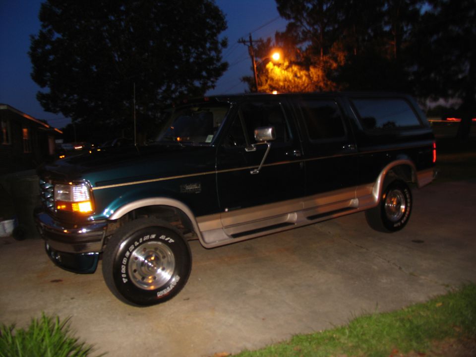 Dark green and tan four-door Ford SUV conversion on polished wheels, side view at dusk