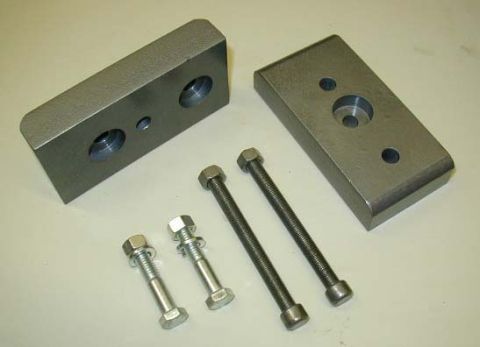 1974 Ford F-100 - Two metal lift blocks and four bolts are laid out on a white surface, likely for vehicle suspension modification.