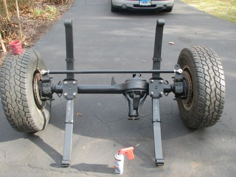 1994 Toyota Tacoma - A rear axle assembly with tires and leaf springs is displayed on a paved surface, with another vehicle visible in the distance.