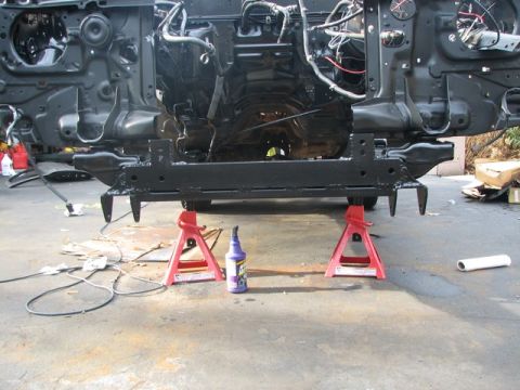 1994 Toyota Tacoma - The front frame section of a vehicle is elevated on red jack stands, revealing the engine bay and suspension components.