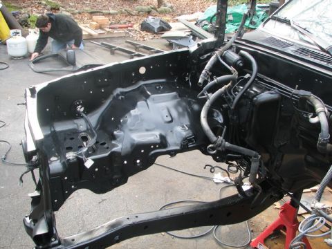 1994 Toyota Tacoma - The engine bay of a truck is shown, with the frame and some hoses visible. A person is cleaning a part in the background.