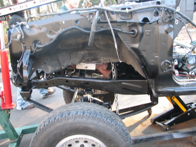 Vehicle frame and engine parts are visible, with a chain attached to the engine. A tire is in the foreground