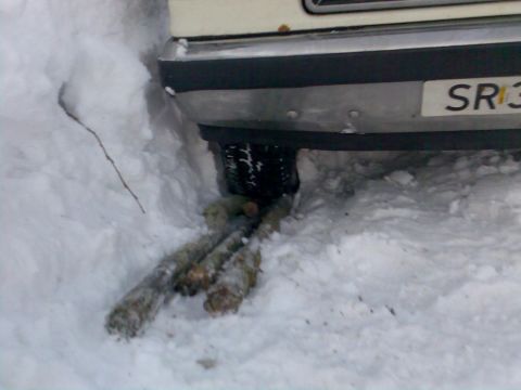 1989 Ford Bronco - A vehicle's rear tire is buried in snow, with logs placed underneath for traction.