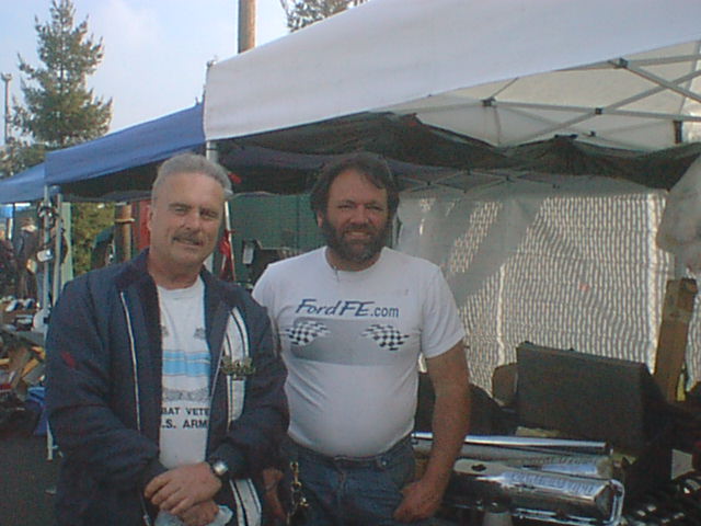 Two men standing at an outdoor swap meet under canopy tents