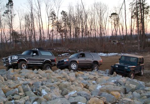 1995 Ford Bronco - Three SUVs are parked on a rocky terrain with trees in the background during sunset.