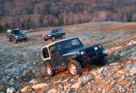1995 Ford Bronco - Three SUVs navigate a challenging, rocky terrain during an off-road excursion.