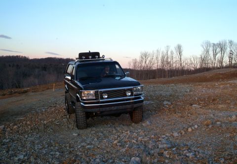 1995 Ford Bronco - A black 1992 Ford Bronco is shown off-road with a roof rack and modified grille.