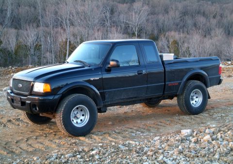 1995 Ford Bronco - Black Ford Ranger Edge pickup truck parked on a dirt road with trees in the background.