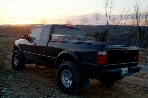 1995 Ford Bronco - Rear three-quarter view of a dark Ford Ranger Edge extended-cab pickup parked on a dirt lot at sunset, with a diamond-plate Kobalt toolbox…