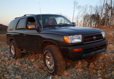 1995 Ford Bronco - This dark SUV is parked on a rocky surface with trees in the background.