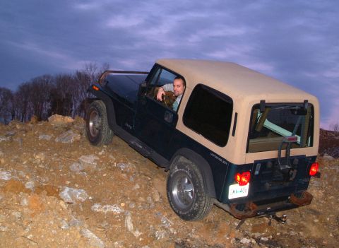 1995 Ford Bronco - Man drives a Jeep Wrangler off-road on a rocky incline under a cloudy sky.