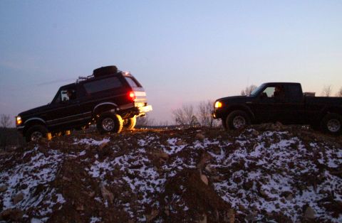 1995 Ford Bronco - Two trucks, a Bronco and a Ranger, navigate a snowy, hilly terrain at dusk.