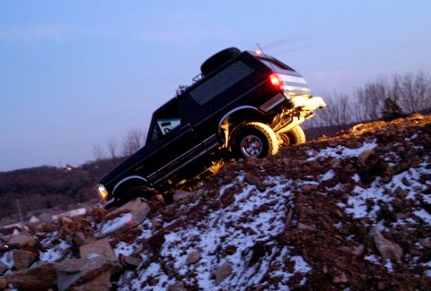1995 Ford Bronco - A black 1995 Ford Bronco navigates a steep, rocky incline covered in patches of snow.