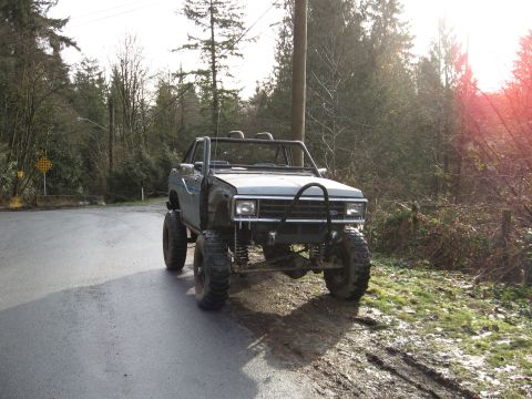 1984 Ford Bronco II - This heavily modified pickup truck is parked on the side of a wet, rural road.