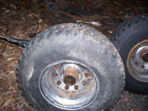 1985 Ford Bronco - Off-road tires and suspension parts are shown resting on the ground, covered in dirt and debris.