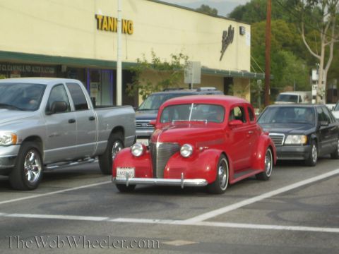 1968 Ford Mustang - A red vintage sedan is seen on the road next to other vehicles.