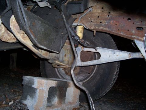 1985 Ford Bronco - The rusty undercarriage of a vehicle, possibly from the 1980s, is visible with suspension parts and a tire resting on cinder blocks.