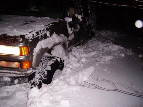 2000 Chevrolet Tahoe - SUV stuck in deep snow, with the front tire buried. The headlight is illuminated.