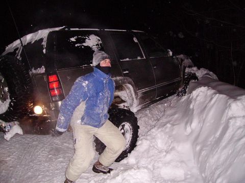 2000 Chevrolet Tahoe - A person stands by a dark-colored SUV that is deeply stuck in a snowdrift at night.
